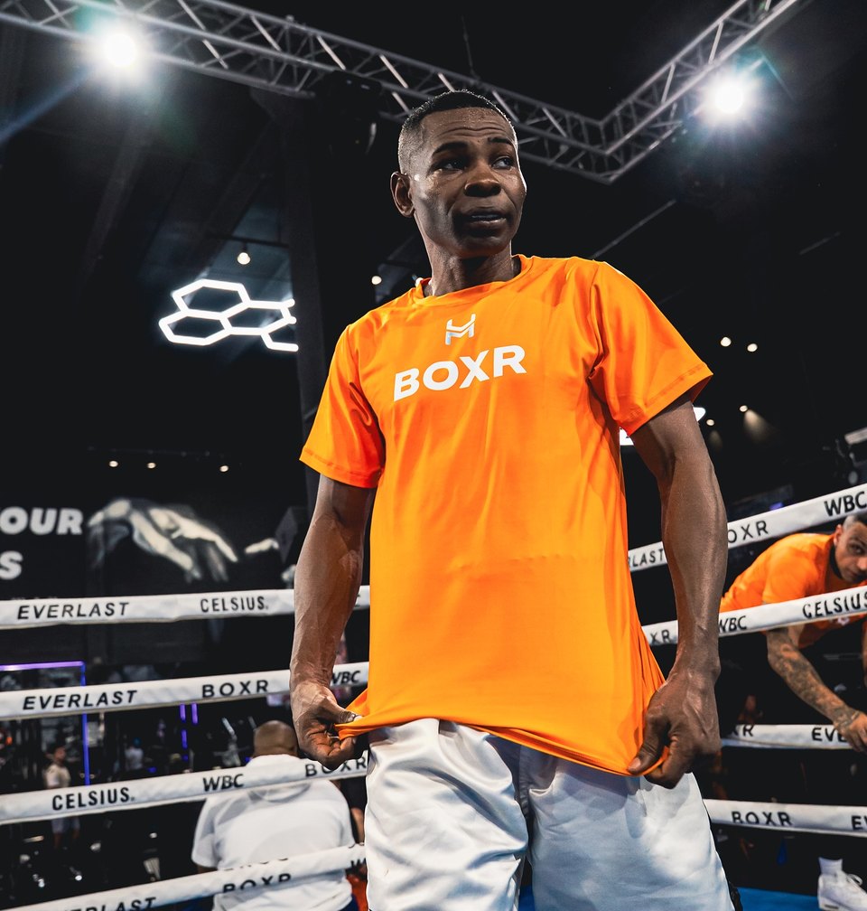 Guillermo Rigondeaux in an orange BOXR tee, standing in the BOXR ring under the truss lights.
