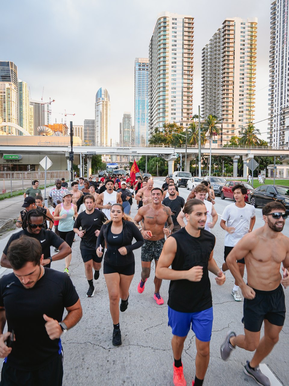 The BOXR Run Club running toward the camera on a downtown street, Edgewater towers and palms behind.